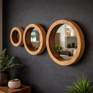 Peut inclure: Trois miroirs ronds en bois de différentes tailles sont accrochés à un mur gris foncé. Les miroirs ont une finition en bois naturel et reflètent la pièce. Le plus grand miroir est à droite, le plus petit à gauche.