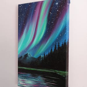 May include: A painting of the aurora borealis over a lake and forest. The sky is a deep blue with streaks of green, purple, and pink light. The trees are silhouetted against the sky, and the lake is reflecting the light of the aurora. The painting is signed "HV 2017" in the lower right corner.
