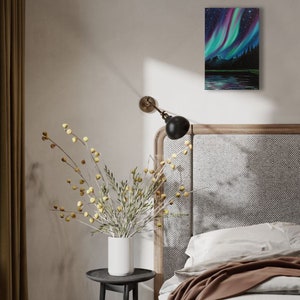 May include: A painting of a dark green forest with a lake reflecting the vibrant green, purple, and blue colors of the aurora borealis in the night sky.