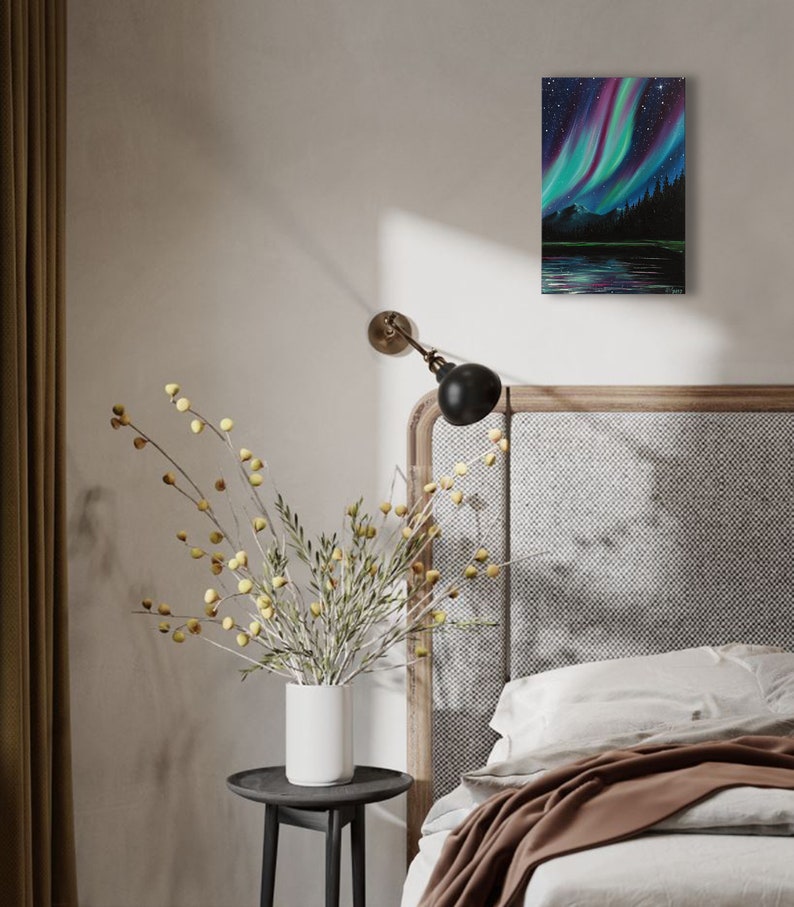 May include: A painting of a dark green forest with a lake reflecting the vibrant green, purple, and blue colors of the aurora borealis in the night sky.
