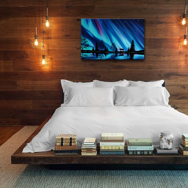 K&ouml;nnte beinhalten: Ein wei&szlig;es Bett mit wei&szlig;en Bettw&auml;sche und einem Holz-Kopfteil. Das Bett steht vor einer Wand mit einem Gem&auml;lde einer blauen und violetten Aurora Borealis &uuml;ber einem See mit B&auml;umen und einer Hirsch-Silhouette. Das Bett hat einen Stapel B&uuml;cher auf dem Nachttisch.