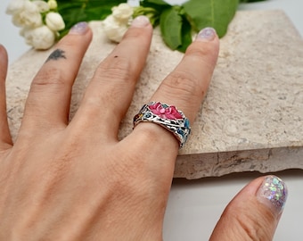 Puede incluir: Un anillo de plata con un diseño de flor de esmalte rosa y azul. El anillo se lleva en un dedo.