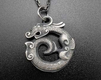 May include: A silver pendant necklace featuring a detailed, coiled dragon design. The dragon is intricately crafted with a textured surface and a circular shape.
