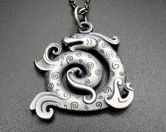 Può includere: Una collana con un ciondolo in argento che presenta un designo di drago avvolto dettagliato. Il drago è arrotolato in un cerchio con la testa rivolta in avanti. Il ciondolo è finemente dettagliato con motivi e trame a spirale.