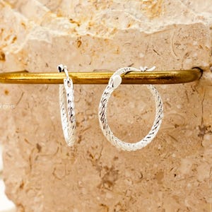 Sterling silver textured hoops catching light and shine