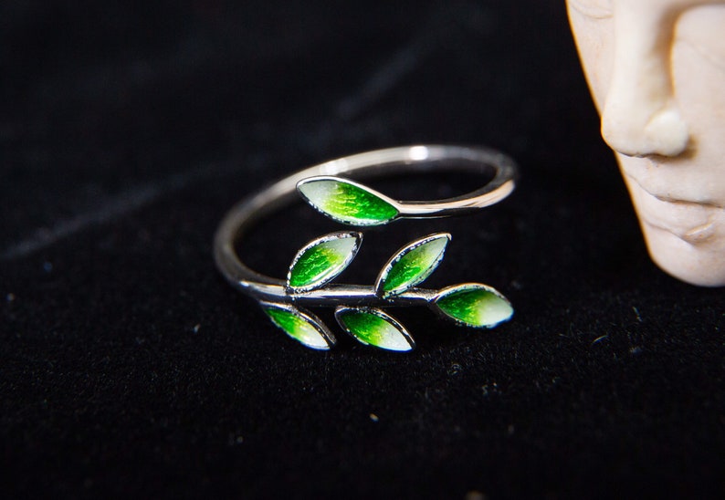 Pode incluir: Um anel de prata com um design de folhas verdes. As folhas s&atilde;o esmaltadas em tons de verde e branco.