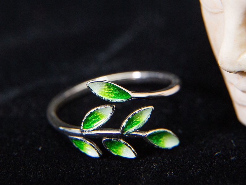 Pode incluir: Um anel de prata com um delicado design de ramo com folhas de esmalte verde. O anel &eacute; ajust&aacute;vel e de extremidade aberta.