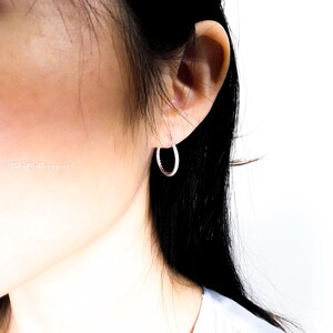 May include: A close-up of a person's ear with a small, silver hoop earring. The earring has a textured surface. The earring is a simple, elegant design. The background is white.