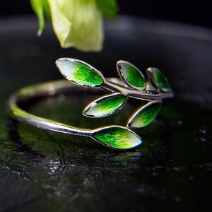 Pode incluir: Um anel de prata com um delicado design de ramo com folhas de esmalte verde.