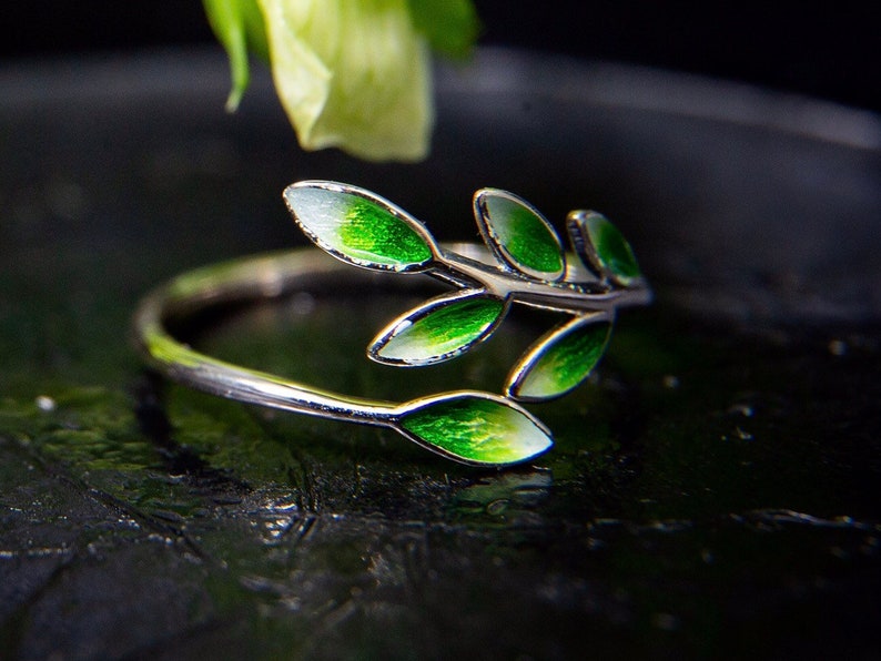 Pode incluir: Um anel de prata com um delicado design de ramo com folhas de esmalte verde.