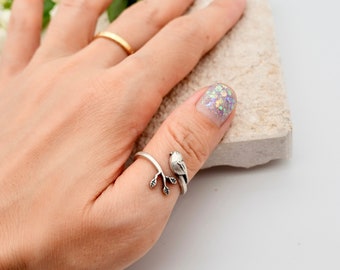 May include: Silver ring featuring a bird perched on a branch. The ring is designed to be worn on the thumb.