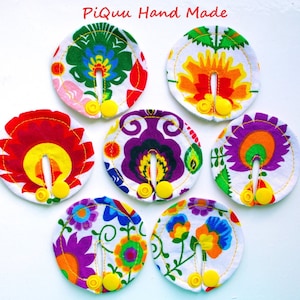 May include: Six colourful fabric circles with a white background and a floral pattern. Each circle has a yellow button and a slit in the centre. The text "Piquu Hand Made" is written in red at the top of the image.