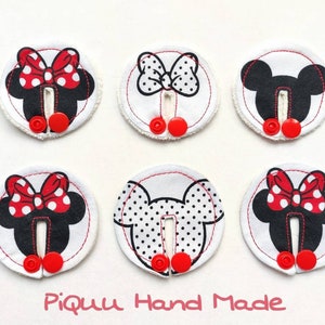 May include: Six round white fabric patches with red and black Mickey Mouse and Minnie Mouse designs. Each patch has two red buttons and a black snap closure.