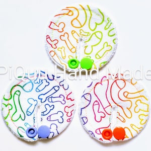 May include: Three round fabric pads with a white background and a rainbow pattern of various shapes. Each pad has a different coloured button in the centre.