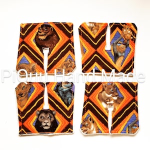 May include: Four fabric coasters with a lion theme. Each coaster features a different lion image set against a geometric pattern of orange, brown, and blue. The coasters have a white border and a cutout in the center.