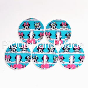 May include: Five circular fabric items with a teal background and a repeating pattern of Minnie Mouse. Each item has a pink button and a slit. The text "Proud Hand Made" is visible in the image.