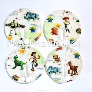 May include: Four circular nursing pads with a Toy Story design. Each pad displays a different character, such as Buzz Lightyear and Woody, on a light green and white patterned background. The pads have a snap closure and a white border.