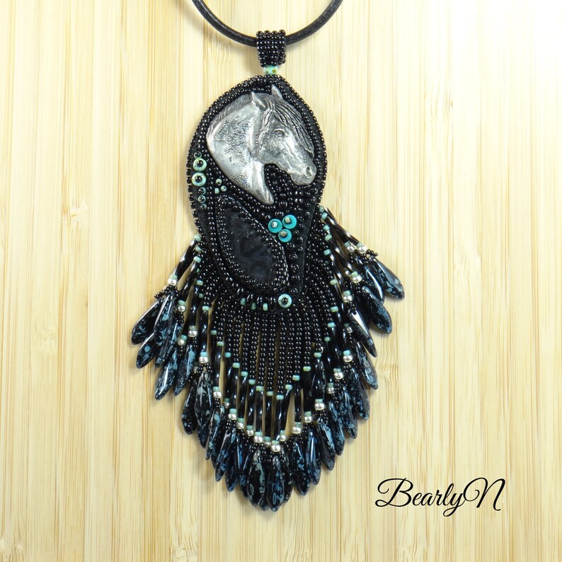 May include: Black beaded necklace with a silver horse head pendant and turquoise accents. The necklace features a long, fringed design.