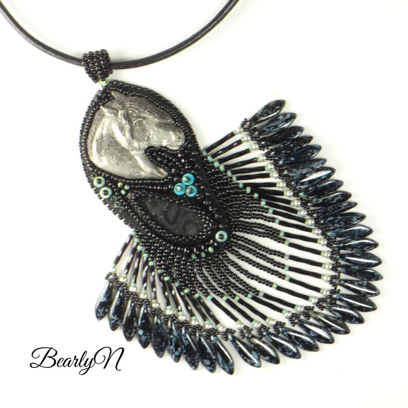 May include: Black beaded necklace with a silver horse head pendant and a black and silver fringe. The fringe is made of small beads and has a black and white speckled pattern.