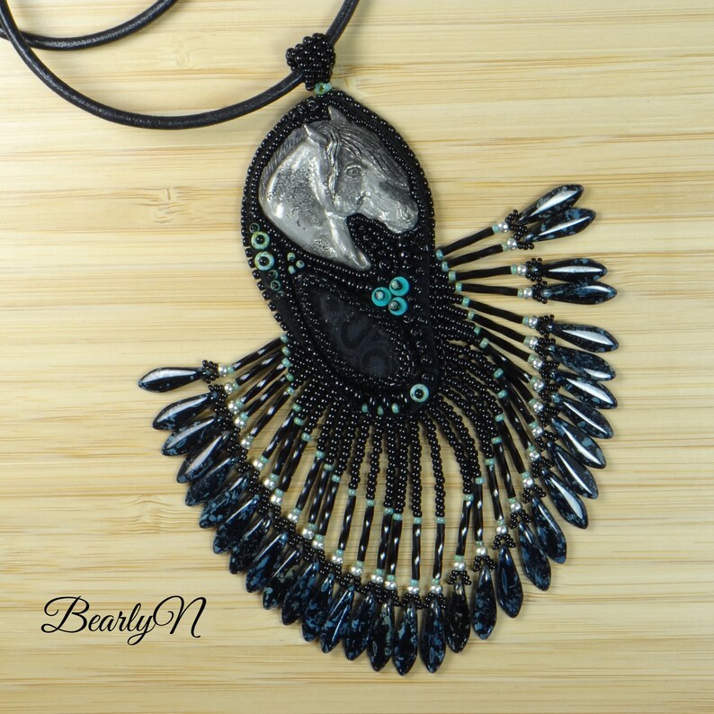 May include: A black beaded necklace with a silver horse head pendant and turquoise accents. The necklace features a fringe of black and blue beads.