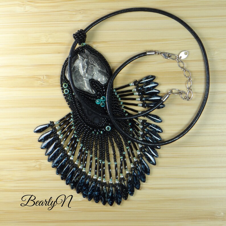 May include: A black beaded necklace with a silver horse head pendant. The necklace features a fringe of black and blue beads.