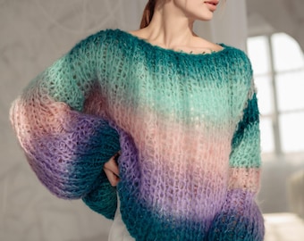 Könnte beinhalten: Eine Frau trägt einen mehrfarbigen Strickpullover mit einem Ombre-Design in Rosa, Lila, Grün und Blau. Sie trägt eine weiße Hose und eine rosa Sonnenbrille.