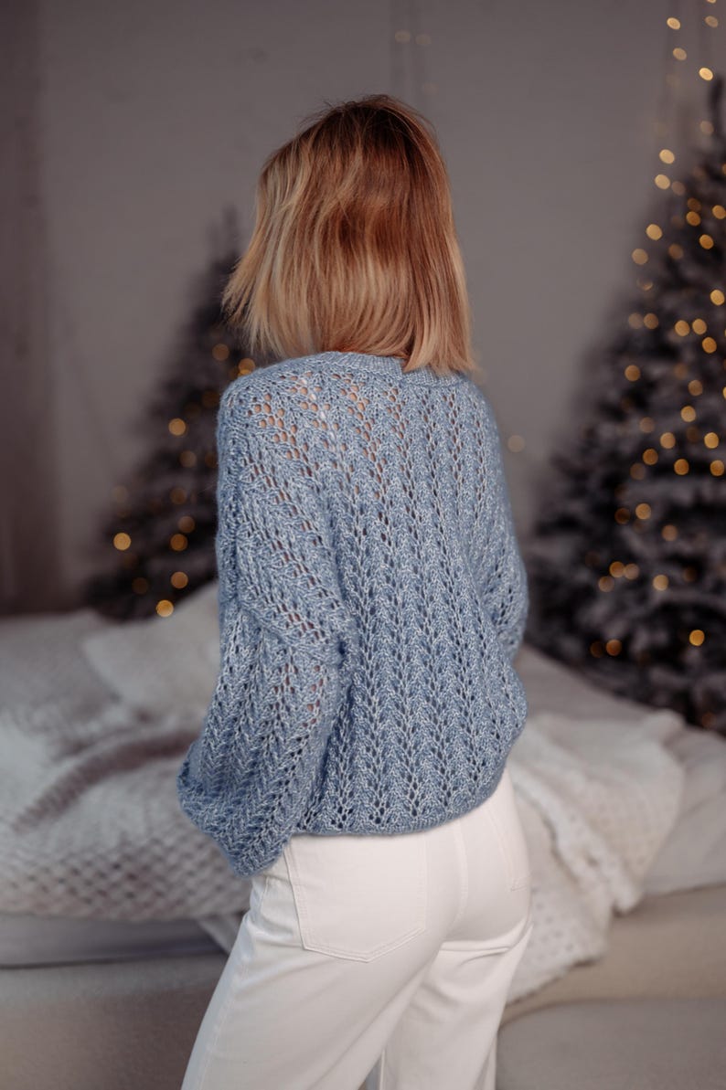 May include: A light blue knitted sweater with a delicate openwork pattern. The sweater has a relaxed fit and long sleeves.