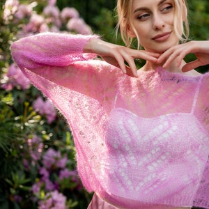 May include: A pink, lacy, lightweight sweater with a loose fit. The sweater is sheer and has a delicate, open-knit design.