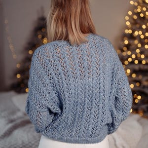 May include: A light blue knitted sweater with a delicate openwork pattern. The sweater has a relaxed fit and a slightly cropped length.