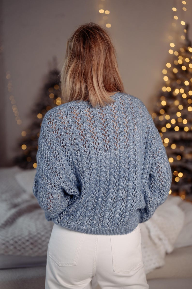 May include: A light blue knitted sweater with a delicate openwork pattern. The sweater has a relaxed fit and a slightly cropped length.