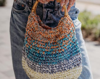 May include: A multi-colored crocheted tote bag with a wooden handle. The bag is made of a variety of colors, including orange, blue, and white.