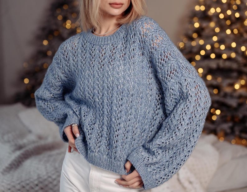 May include: A light blue knitted sweater with a delicate openwork pattern. The sweater has long sleeves and a relaxed fit.