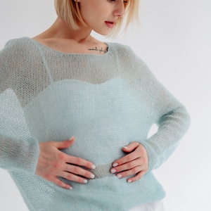 May include: A light blue, sheer knit sweater with a loose fit and long sleeves. The sweater is made of a soft, delicate material and has a relaxed, casual style.
