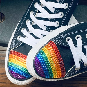 May include: A pair of black canvas sneakers with a rainbow-colored rhinestone design on the toe. The rhinestones are arranged in a rainbow pattern.