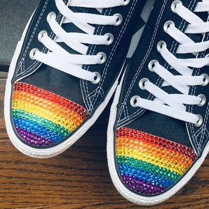 May include: A pair of black canvas sneakers with white laces and a rainbow-colored rhinestone design on the toe.