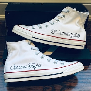 Puede incluir: Un par de zapatillas blancas de lona de ca&ntilde;a alta con ribetes rojos. Un zapato est&aacute; personalizado con el texto "10th January 2019" y el otro zapato est&aacute; personalizado con el texto "Syvana Taylor".
