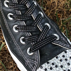 May include: Black leather high-top sneakers with white laces and a white rubber sole. The toe of the shoe is covered in rhinestones.