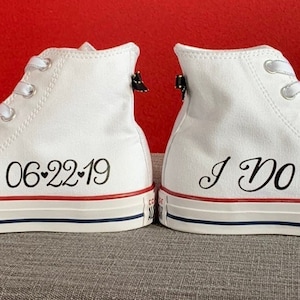 Puede incluir: Un par de zapatillas blancas de ca&ntilde;a alta con cordones negros. Un zapato dice "06-22-19" con un s&iacute;mbolo de coraz&oacute;n y el otro zapato dice "S&iacute;, quiero".
