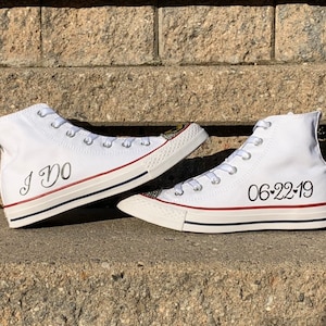 Puede incluir: Un par de zapatillas blancas de ca&ntilde;a alta con escritura negra. Un zapato dice "I Do" y el otro dice "06-22-19".