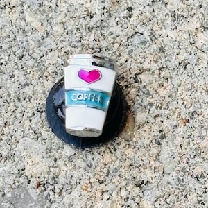 May include: A white coffee cup charm with a pink heart and blue trim. The charm says "Coffee" on the side.