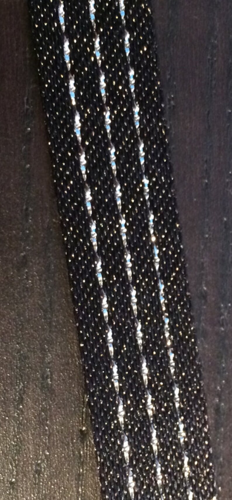 May include: A close-up of a black beaded bracelet with silver accents. The bracelet is made of small, round beads that are strung together in a tight pattern. The silver accents are small, shiny beads that are interspersed throughout the black beads.