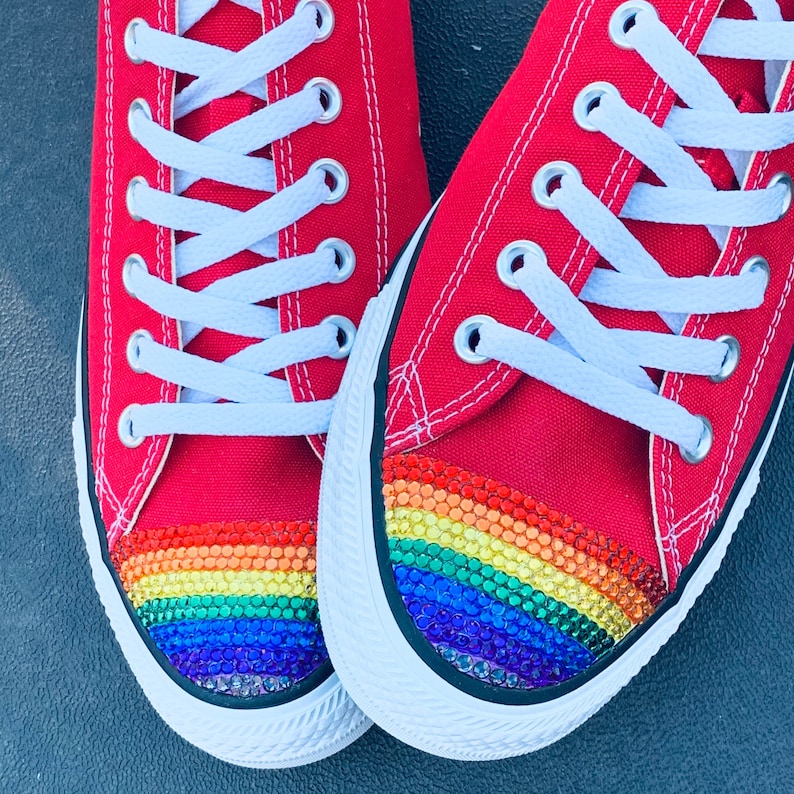 May include: A pair of red canvas sneakers with white laces and a rainbow-colored rhinestone design on the toe.