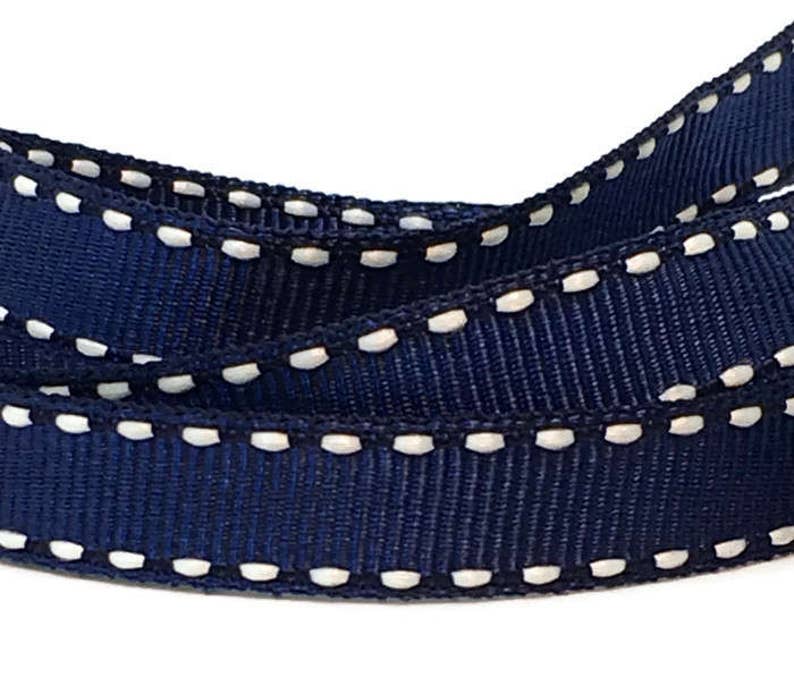 May include: Navy blue ribbon with a white stitched edge. The ribbon is folded in half, showing the stitching on both sides.