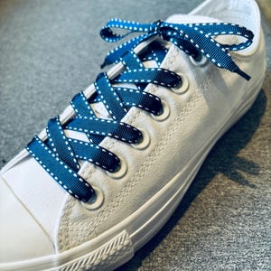 May include: White canvas sneakers with navy blue shoelaces featuring white polka dots. The shoelaces are tied in a criss-cross pattern.