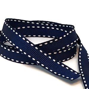 May include: Navy blue ribbon with white stitching along the edges. The ribbon is folded in half and the stitching is visible on both sides.