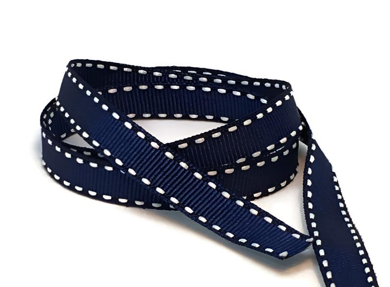 May include: Navy blue ribbon with white stitching along the edges. The ribbon is folded in half and the stitching is visible on both sides.