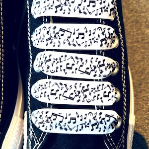 May include: Black canvas shoes with white shoelaces featuring a repeating pattern of musical notes.
