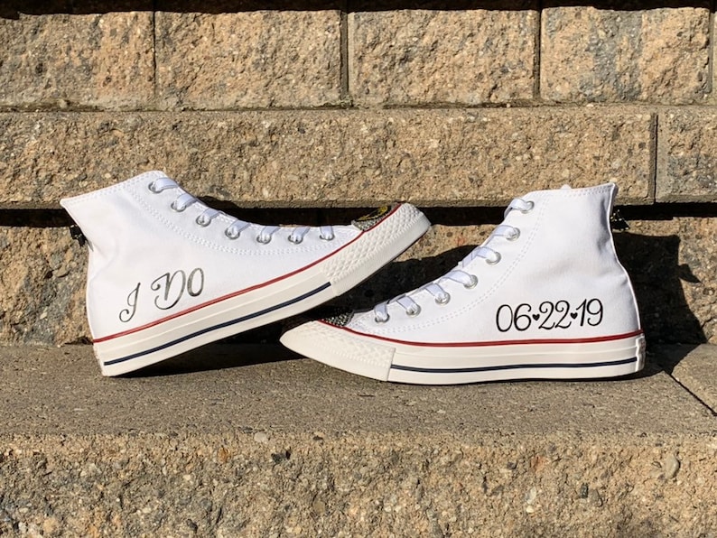 Puede incluir: Un par de zapatillas blancas de ca&ntilde;a alta con escritura negra. Un zapato dice "I Do" y el otro dice "06-22-19".