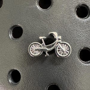 May include: A silver charm in the shape of a bicycle. The charm has a detailed design with two wheels, handlebars, and a seat.