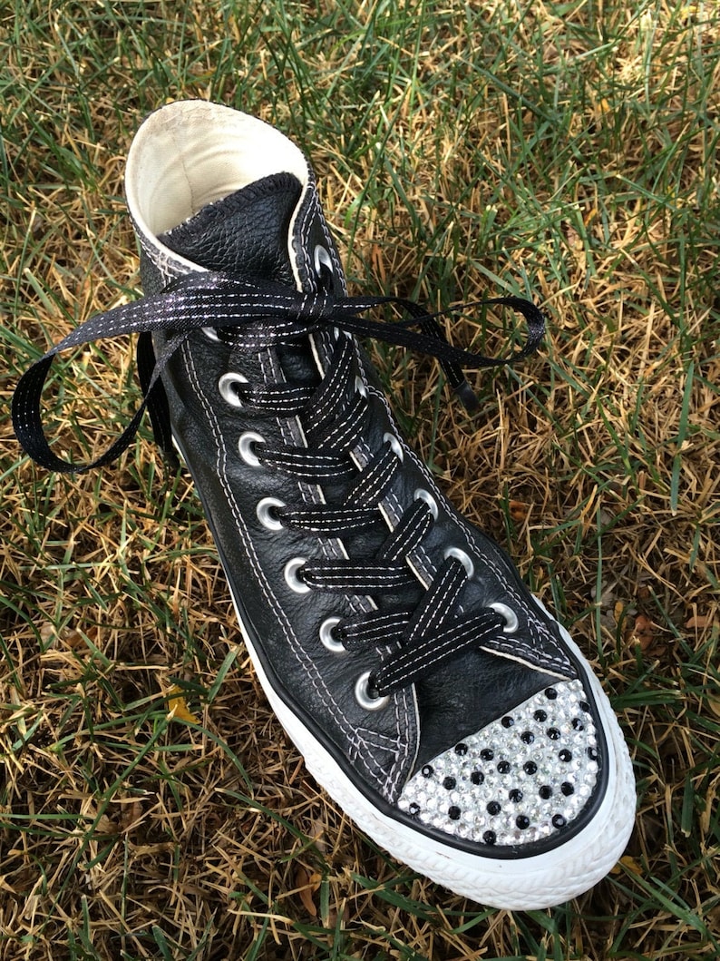 May include: Black leather high-top sneakers with white laces and a white rubber sole. The toe of the shoe is covered in rhinestones.
